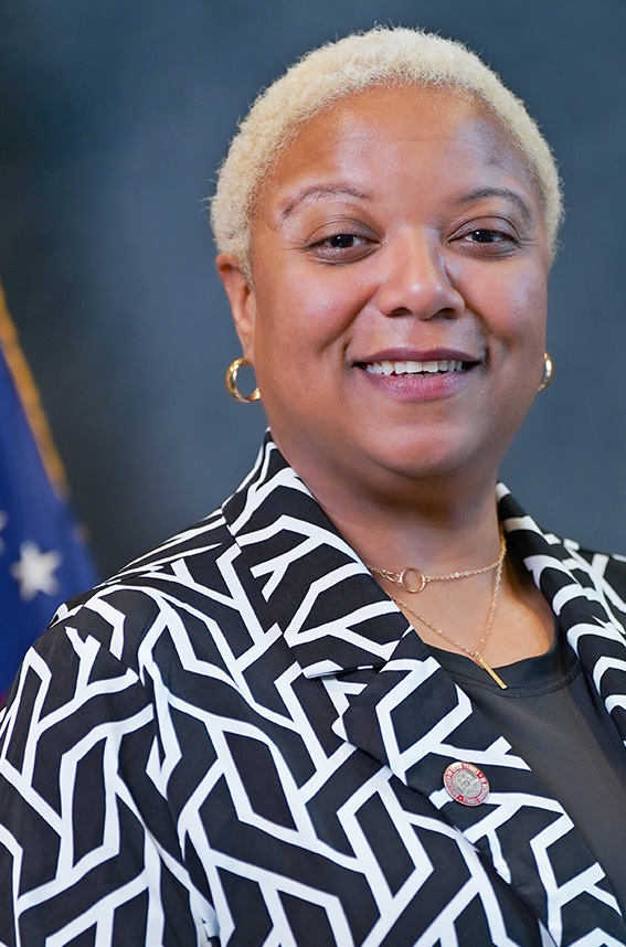 Black female wearing glasses a black jacket and pink shirt 
